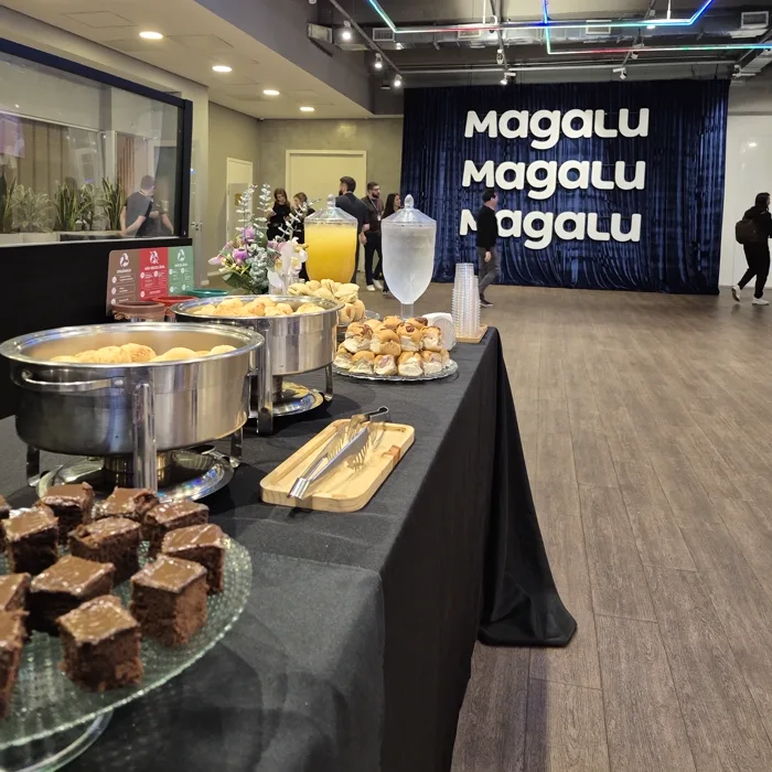 Buffet montado em evento corporativo, com réchauds, doces e pães de queijo prontos antes da abertura