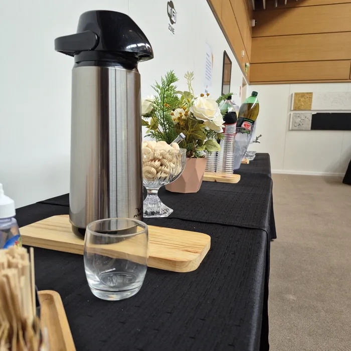 Estação de café montada: garrafa térmica, copos e arranjo de flores sobre a mesa